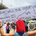 Pipeline protestor holds sign that says, "What will the state do? How much is enough power and profit? We are watching you."