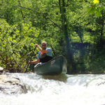 man in a canoe goes over a rapid