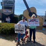 two people in front of a large guitar statue hold signs about the landfill problems