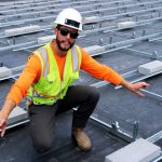 A project manager in a neon vest and construction hat kneels atop the roof of the St. Paul school..