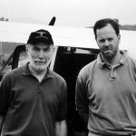 Two men stand outside a small plane