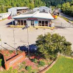 An aerial photo shows a business called Breeding's Plumbing & Electric. A brick sign and three flags stand on the opposite side of the parking lot.