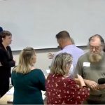 People stand in a room with a whiteboard covering the wall behind them